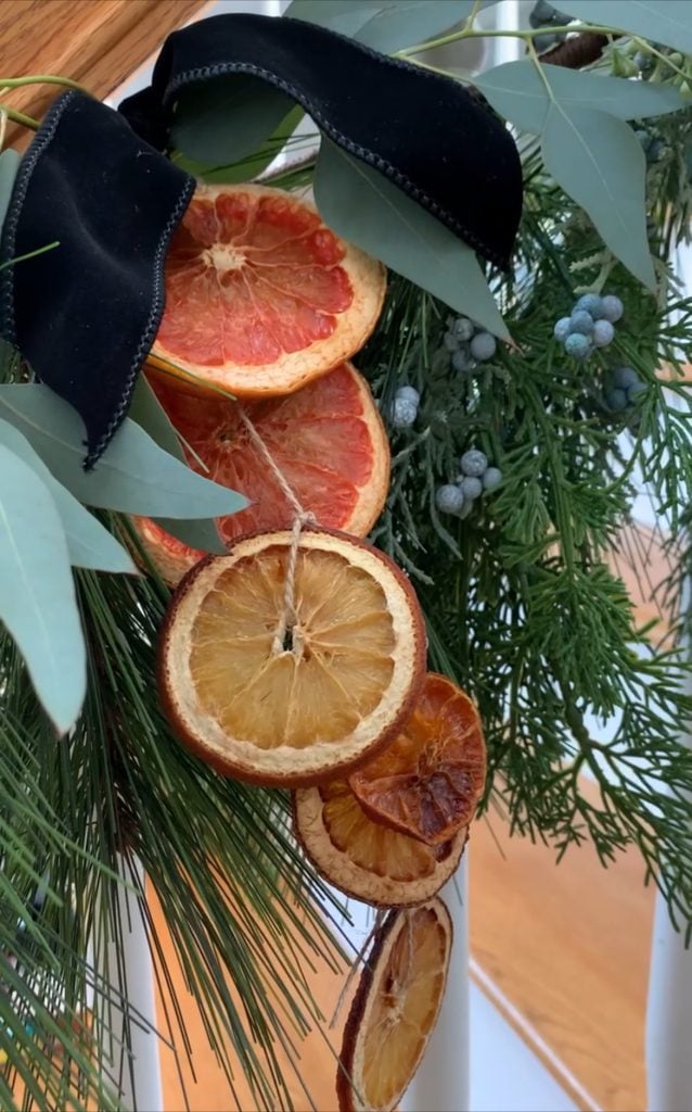 A decorative arrangement of dried citrus slices hangs with greenery and a black ribbon on a staircase railing.