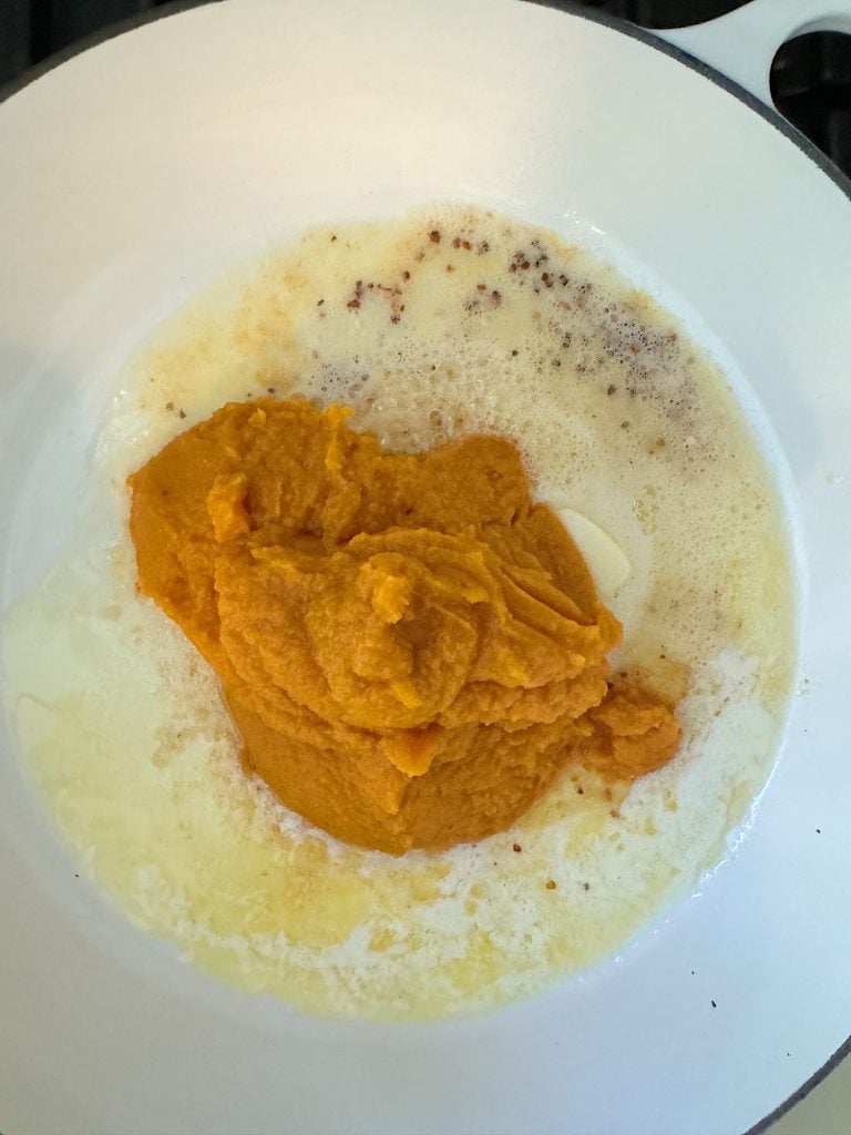 Pumpkin puree cooking in a white pan with melted butter.