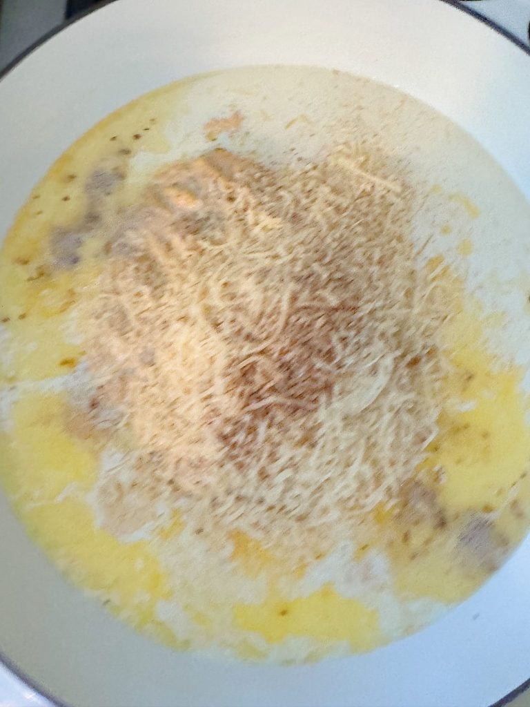 A pan containing grated cheese melting in a mixture of butter and cream.