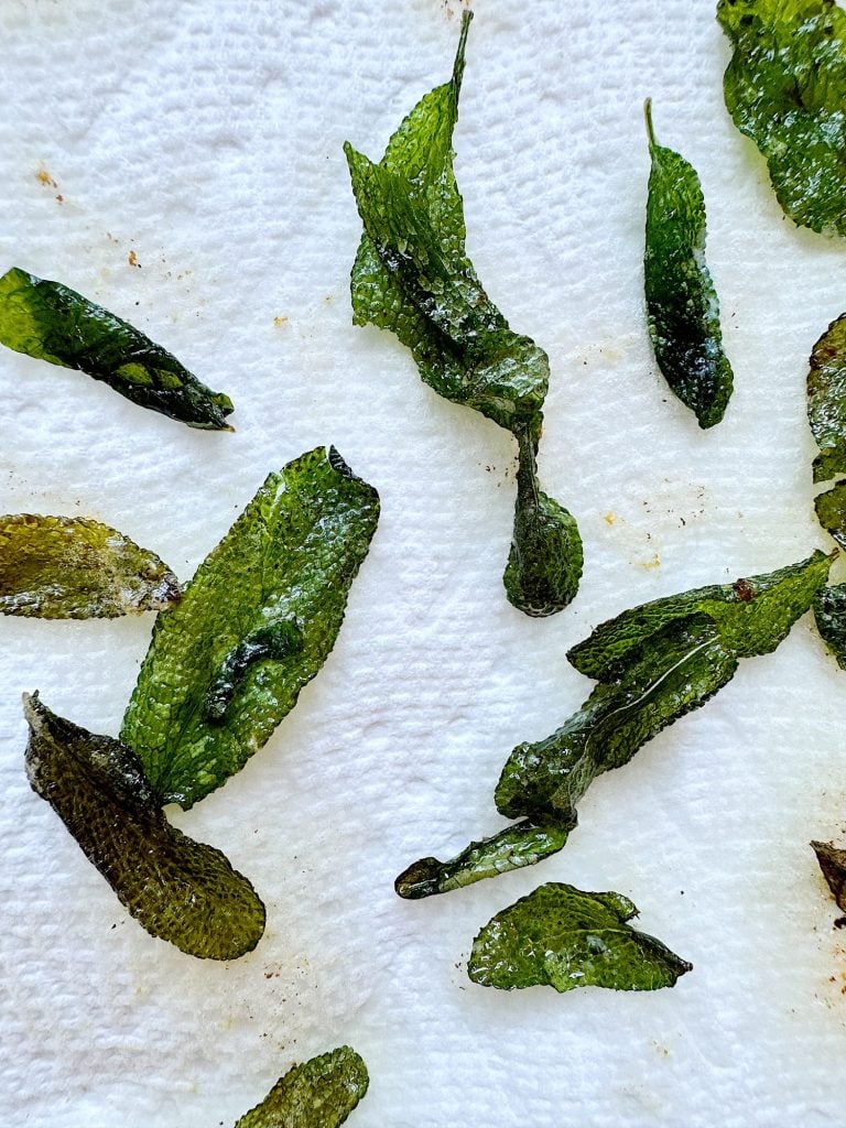 Close-up of crispy fried sage leaves on a white paper towel.