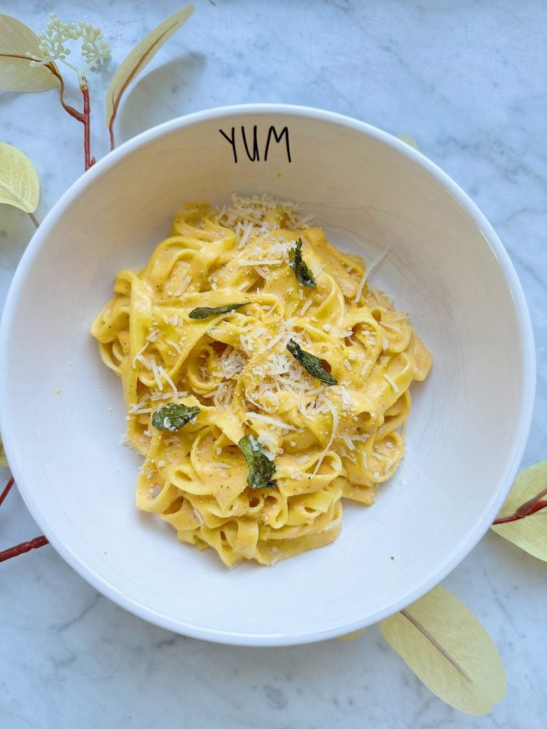 A bowl of pasta topped with grated cheese and herbs, placed on a marble surface. The bowl has "YUM" written on its rim.