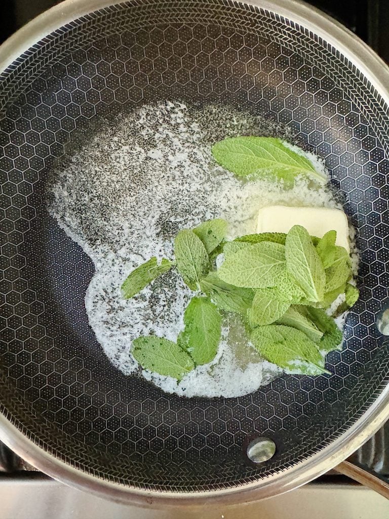 Butter melting with fresh mint leaves in a frying pan.