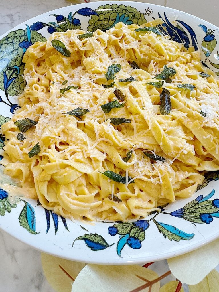 A plate of creamy pasta topped with grated cheese and fresh herbs on a decorative dish.