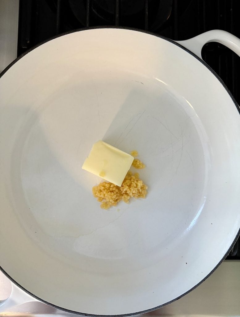 A pat of butter and minced garlic in a white pan on a stovetop.