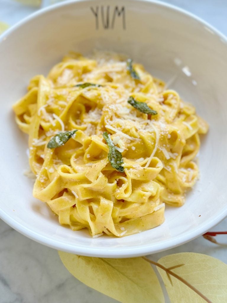 A bowl of fettuccine pasta topped with creamy sauce, grated cheese, and garnished with fresh basil leaves. The bowl has "YUM" written on the inside rim.