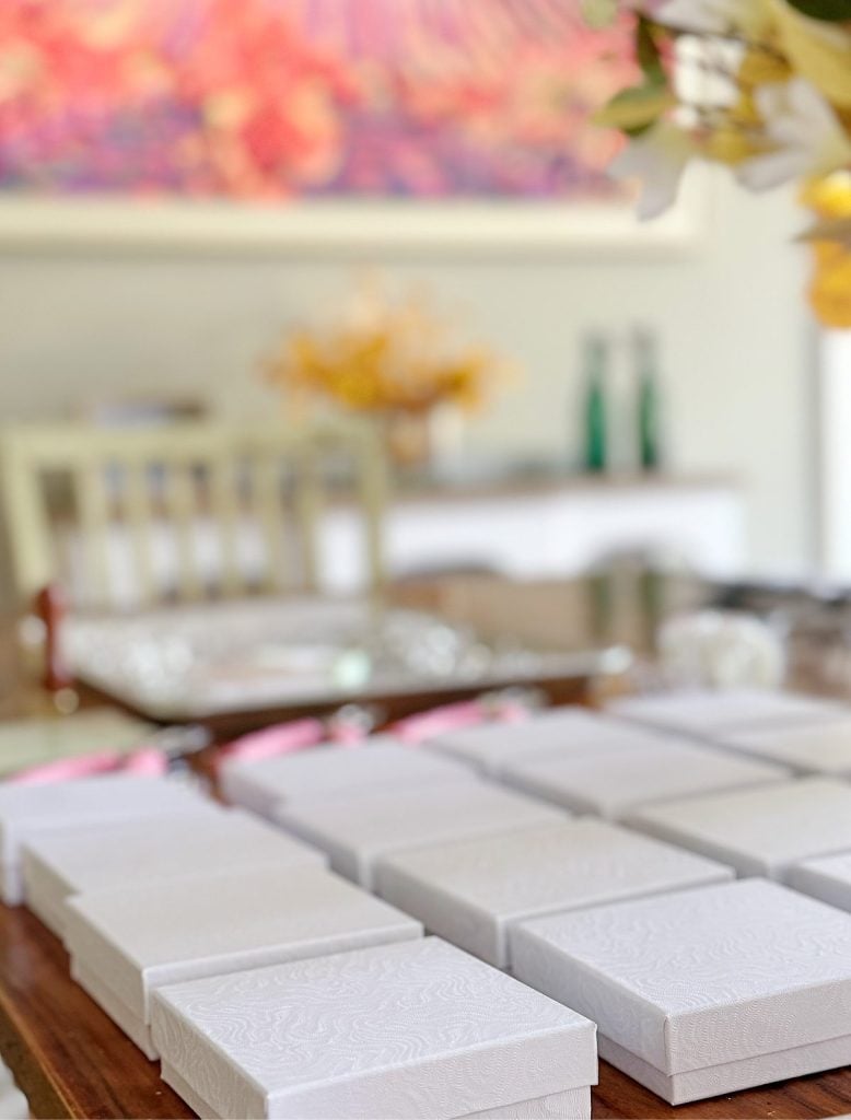 A table with neatly arranged white gift boxes, blurred background with flowers and abstract art.