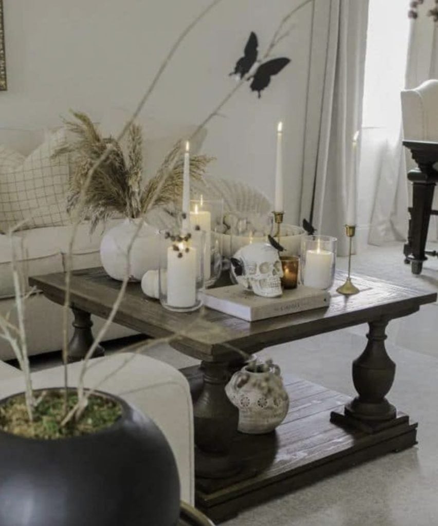 A wooden coffee table with candles, a skull decoration, and dried plants, set in a neutral-toned living room.