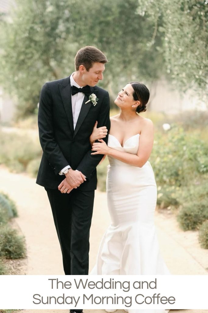 A couple dressed in formal wedding attire, walking arm in arm on a garden path.