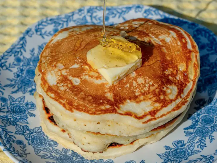 A stack of pancakes topped with a pat of butter and drizzled with honey, served on a blue floral-patterned plate.