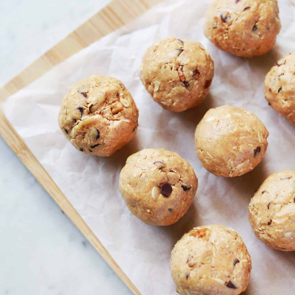 Nine round cookie dough balls with chocolate chips and nuts on parchment paper.