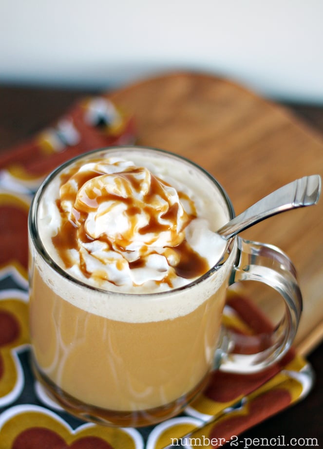 A mug of coffee topped with whipped cream and caramel drizzle, placed on a patterned napkin with a spoon inside.