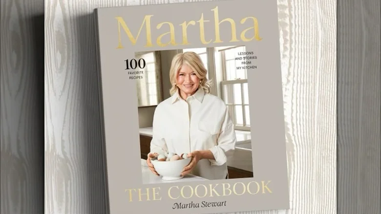 Cover of "Martha: The Cookbook" featuring a person holding a bowl in a kitchen setting, with text highlighting "100 Favorite Recipes.