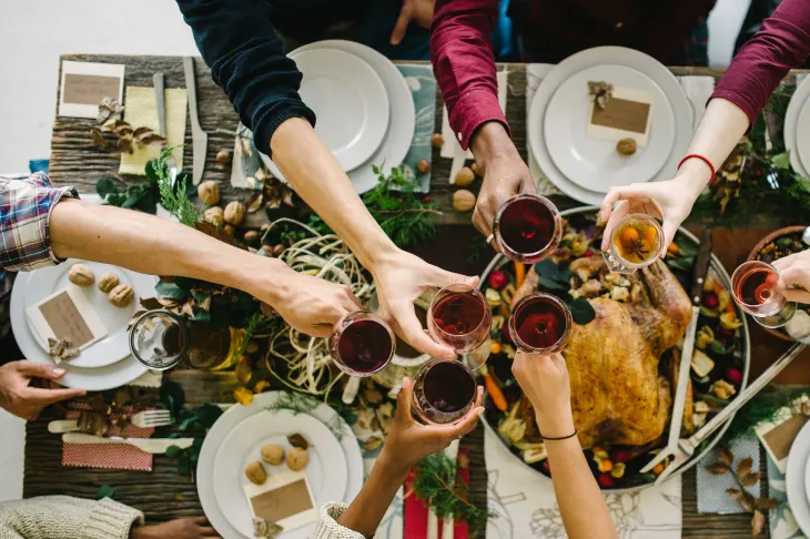 A group of people clinking glasses over a dinner table with a roast turkey and various dishes.