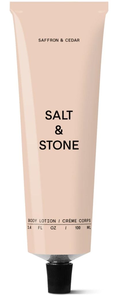 A beige tube labeled "Salt & Stone" saffron & cedar body lotion, 3.4 fl oz (100 ml), with a black screw cap—its comforting scent evokes the warmth of Christmas Morning.