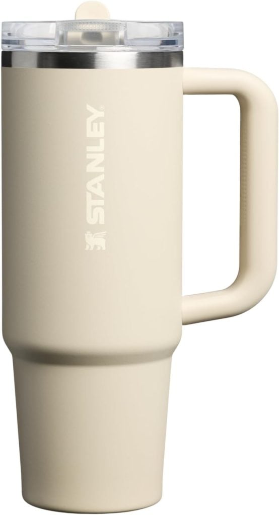 A beige Stanley travel tumbler with a handle and a clear lid, perfect for sipping coffee on Christmas morning, shown against a white background.