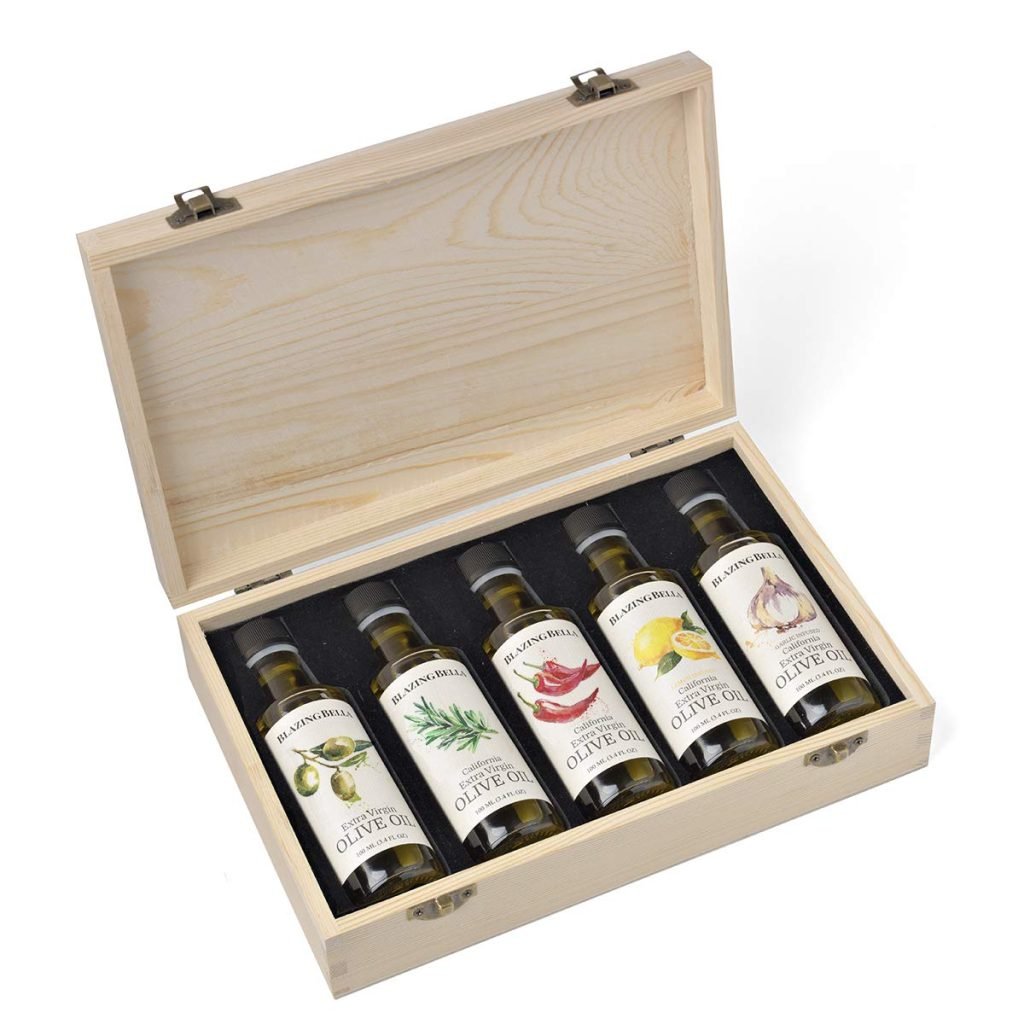 A wooden box containing five bottles of flavored olive oil with different labels, including herbs and chili, neatly arranged inside.