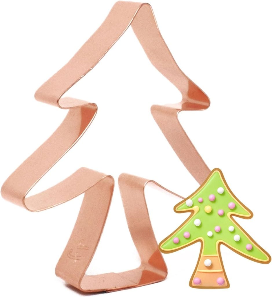 A copper tree-shaped cookie cutter sits elegantly beside a small, beautifully decorated tree-shaped cookie, perfect for crafting delightful holiday desserts.