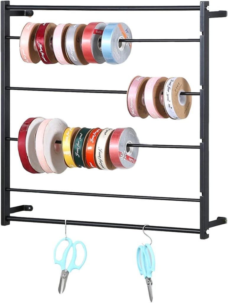 A wall-mounted metal rack, perfect for gift wrapping, organizes various rolls of ribbon on three rods, with two pairs of scissors hanging from hooks below.