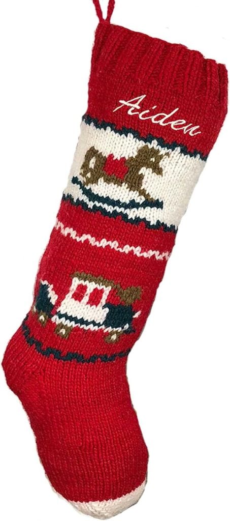 Red knit Christmas stocking with white and green patterns, featuring a rocking horse and toy train design—the perfect touch for a festive Christmas morning, with the name "Aiden" stitched at the top.