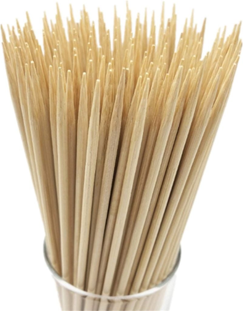 A glass container holds numerous wooden skewers with sharp pointed tips facing upward.