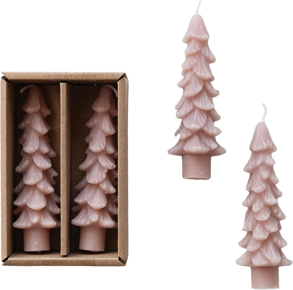 Two pink, tree-shaped candles evoke a pink Christmas vibe as they are displayed in a cardboard box, with two identical candles positioned outside the box on a white background.