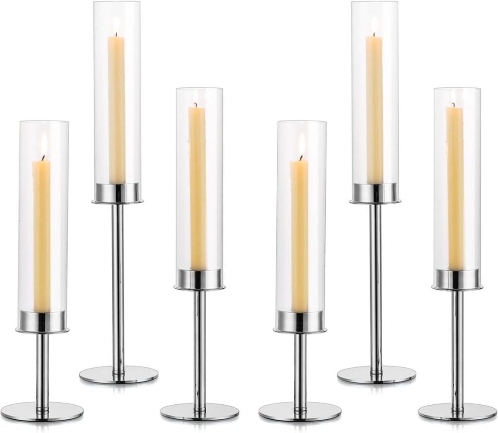 Seven tall, cylindrical glass candleholders with metal bases, each containing a lit, slender beige candle reminiscent of subtle Christmas colors.