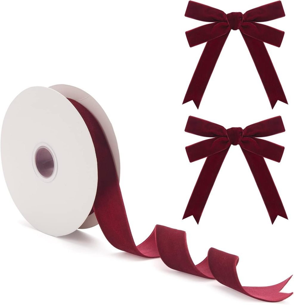 A roll of burgundy ribbon, a staple among Christmas colors, is unraveled next to two tied bows of the same festive hue.