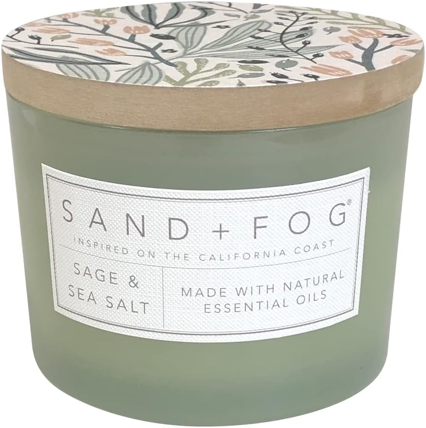 A frosted glass candle labeled "Sand + Fog Sage & Sea Salt," featuring a floral-patterned wooden lid and natural essential oils—perfect for capturing the fresh, invigorating spirit of Christmas Morning.