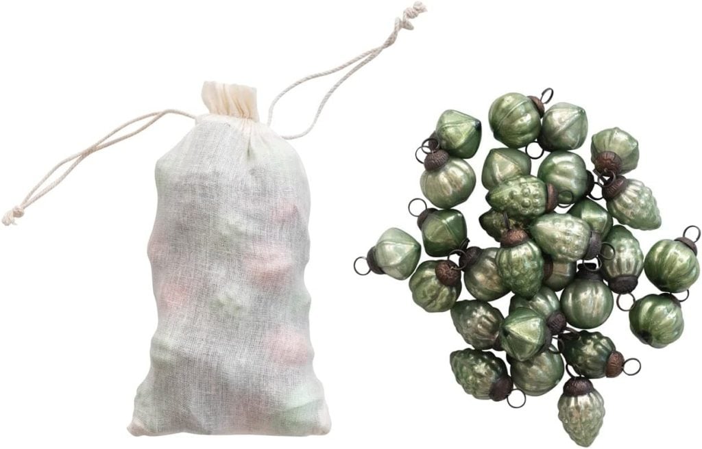 A drawstring bag sits next to a pile of small, green, acorn-shaped ornaments with loops for hanging, perfectly capturing the essence of Christmas colors.