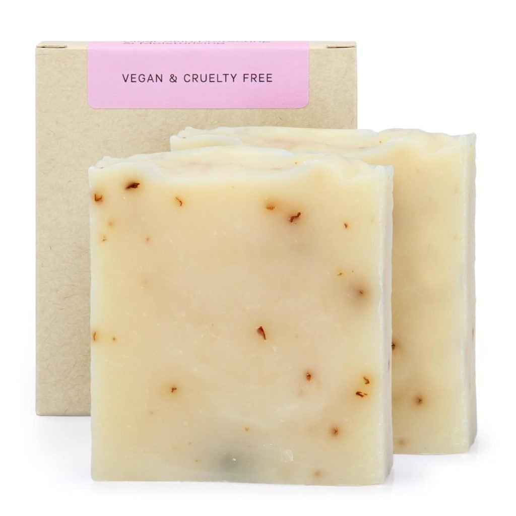 Two handmade soap bars with specks, labeled "Vegan & Cruelty Free," in front of a plain cardboard box.