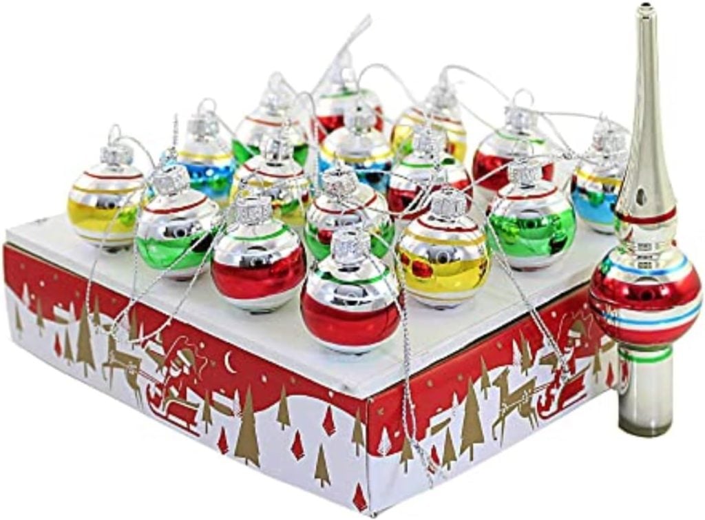 A set of colorful, shiny Christmas ornaments and a tree topper sit on a decorative box adorned with red and white holiday themes, accented by a festive Christmas ribbon.