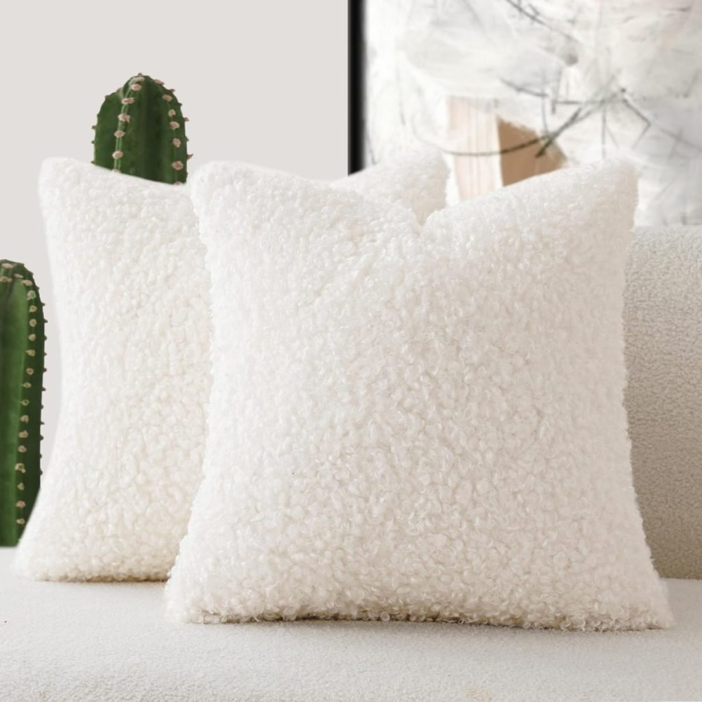 Two fuzzy white pillows on a light-colored couch complement the vibrant Christmas colors of the cactus plant in the background.