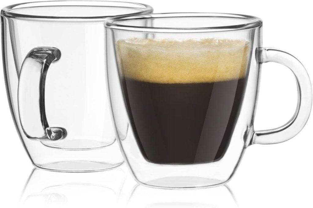 Two clear glass cups, one brimming with rich Black Friday espresso and foam, the other empty, sit side by side on a pristine white surface.