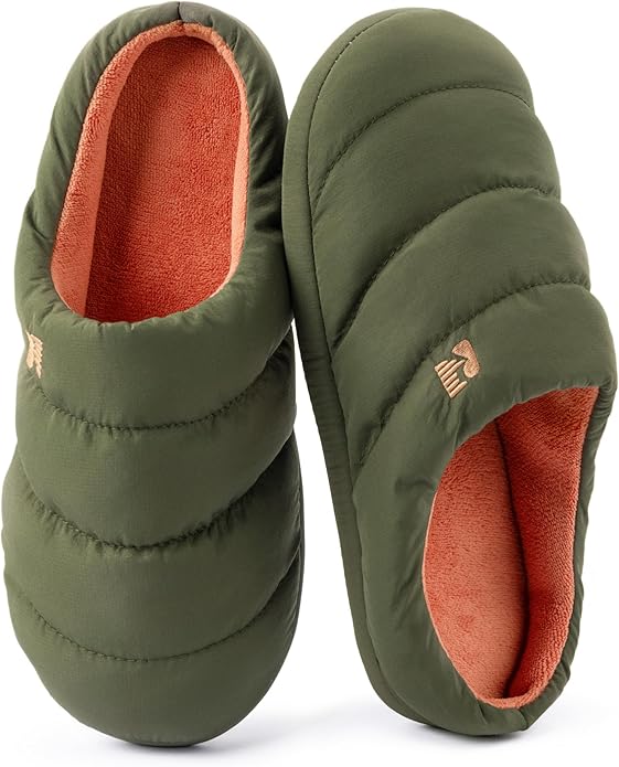 A pair of green quilted slippers with orange lining, reminiscent of Christmas morning coziness, one upright and one laying on its side, displayed on a white background.