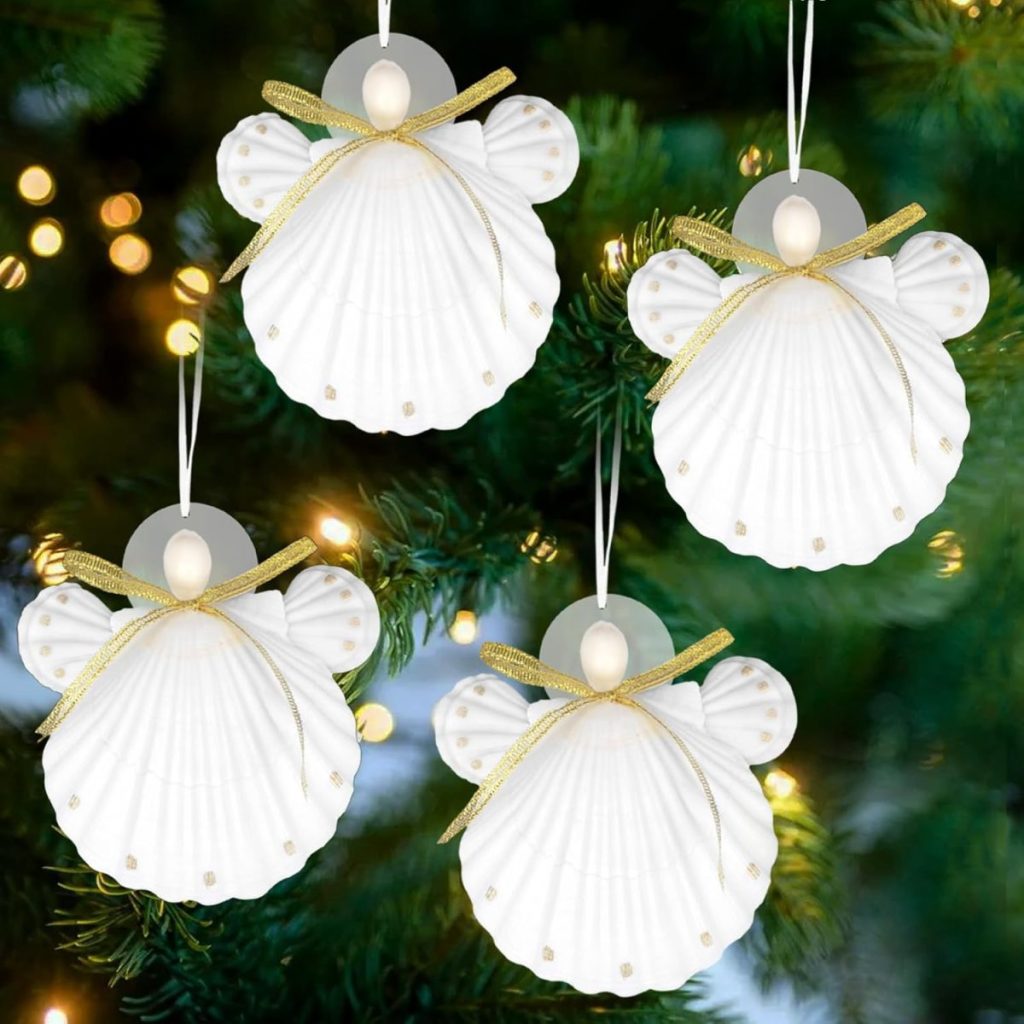 Four delicate oyster shell angel ornaments with gold ribbons hang gracefully on a Christmas tree, surrounded by twinkling fairy lights.