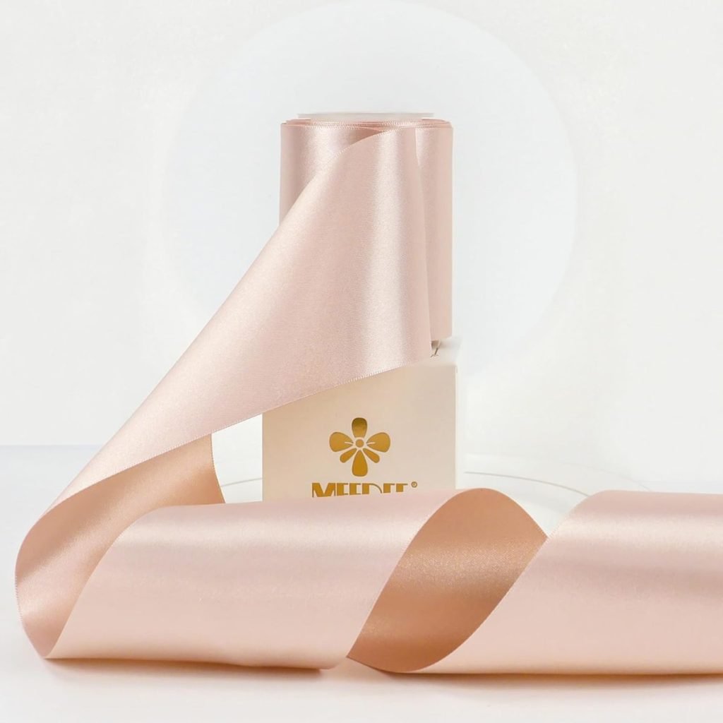 A bottle with a gold logo wrapped in glossy, pale pink ribbon tied gracefully in a bow on a white background.