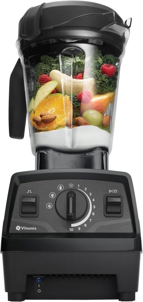 A Vitamix blender, reminiscent of a nutcracker's precision at Christmas, is filled with fruits, vegetables, and nuts. It sits elegantly on a black base with intuitive control dials, ready to create festive blends.