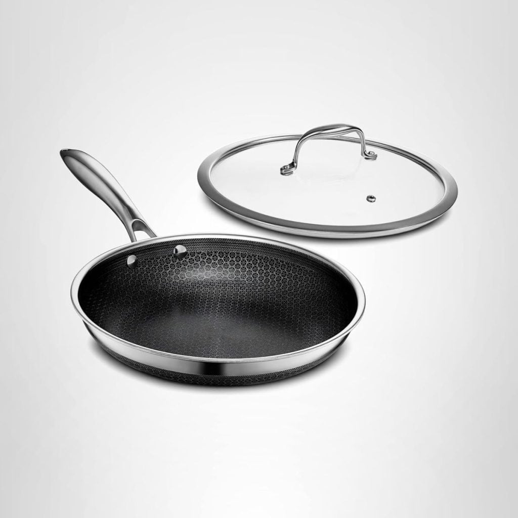 A nonstick frying pan with a textured interior and a metal handle is shown next to a matching glass lid with a metal rim and handle, recalling the charm of Vintage Christmas Ornaments in its timeless, classic design.