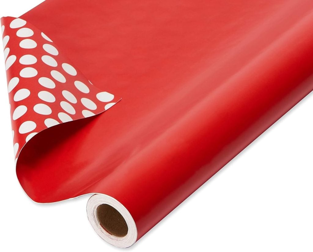 A roll of red wrapping paper, perfect for gift wrapping, partially unrolled to reveal a charming white polka dot pattern on the reverse side.