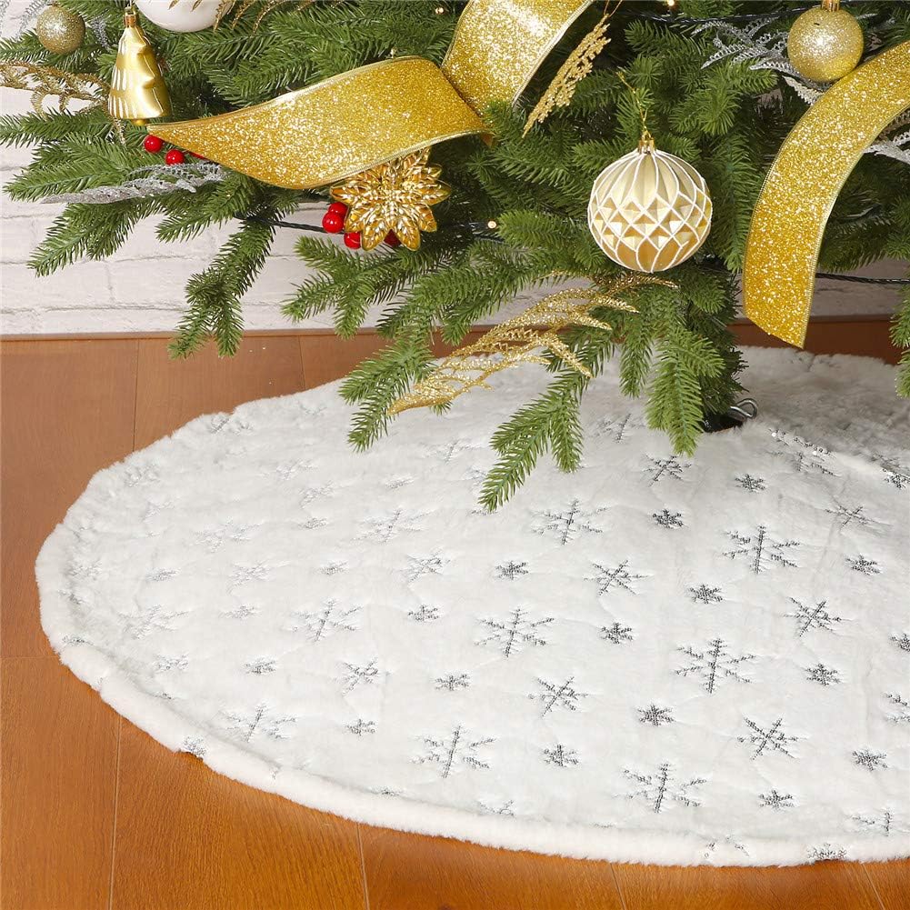 A Christmas tree adorned with gold ribbon and ornaments stands elegantly, its evergreen needles complemented by a luxurious christmas tree skirt embellished with silver snowflakes on a wooden floor.