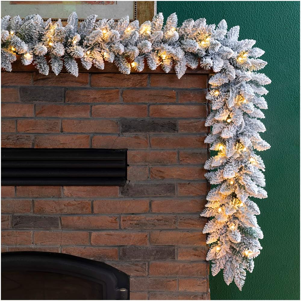 A garland of snow-covered Christmas colors and twinkling lights decorates a brick fireplace against a green wall.