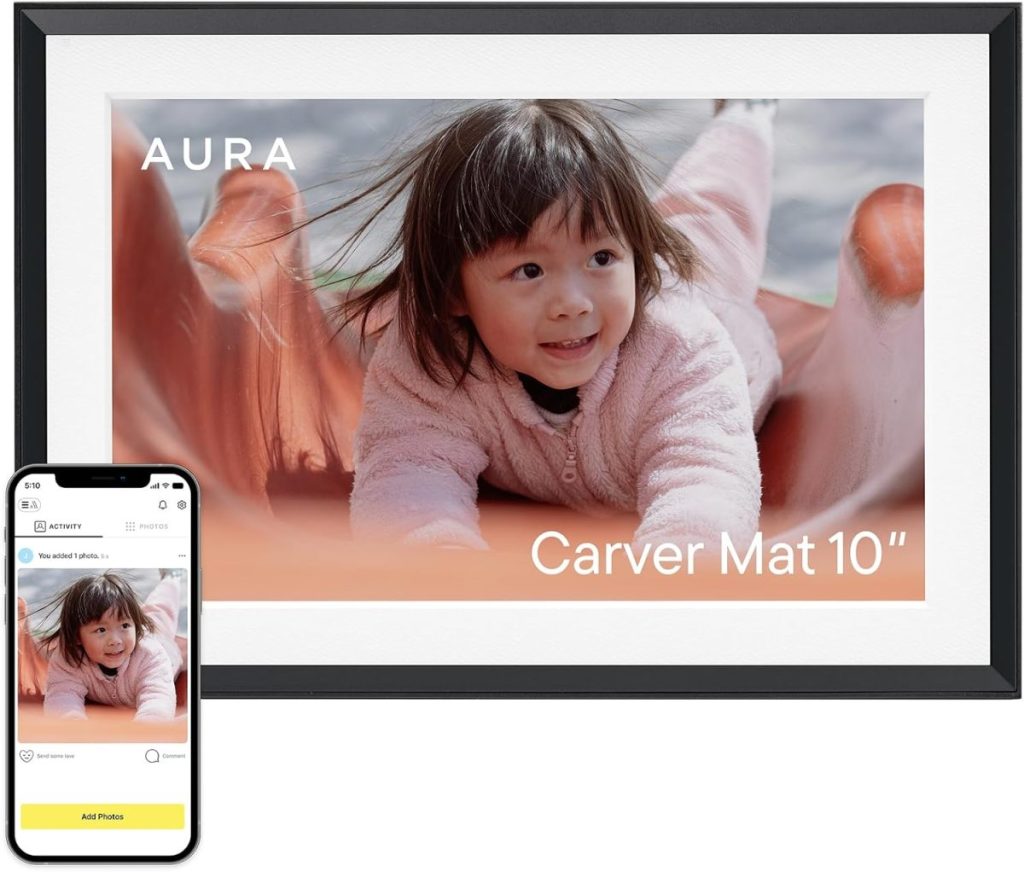 A digital photo frame displaying a young child sliding, with a smartphone beside it showing the same photo and the Aura app interface. Text reads "AURA Carver Mat 10''—the perfect Black Friday gift for sharing special moments.