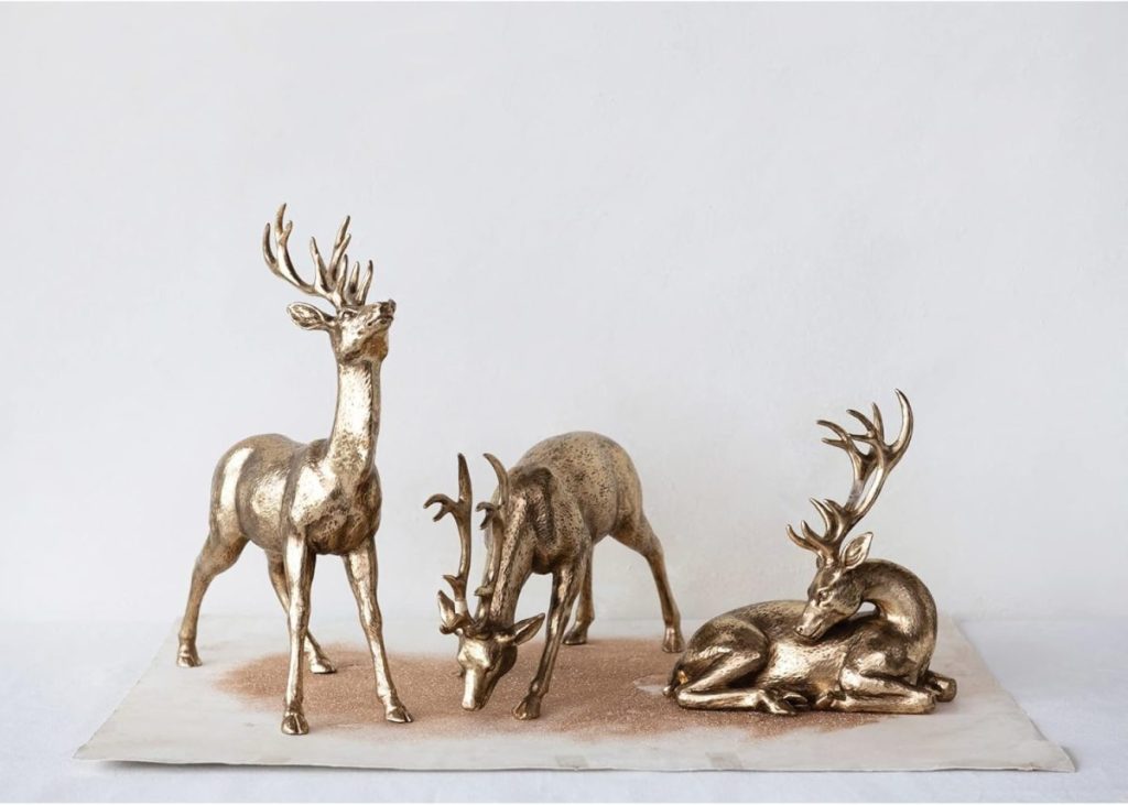 Set a Christmas table with these three metallic deer figurines: one standing, one grazing, and one lying down, creating an elegant and festive display.