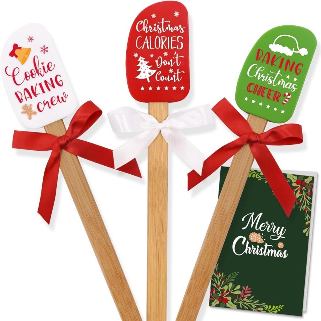 Three festive spatulas with Christmas-themed text and bows, perfect for preparing Christmas tree cupcakes, alongside a "Merry Christmas" card.