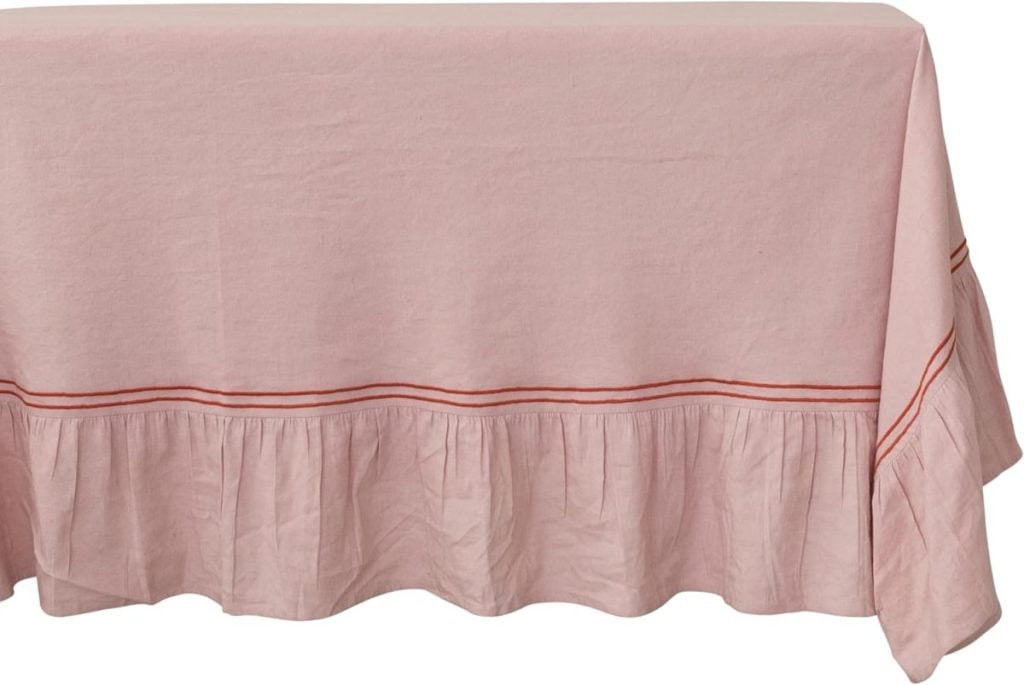 A rectangular table covered with a light pink Christmas tablecloth featuring a ruffled edge and a thin red stripe near the ruffle.