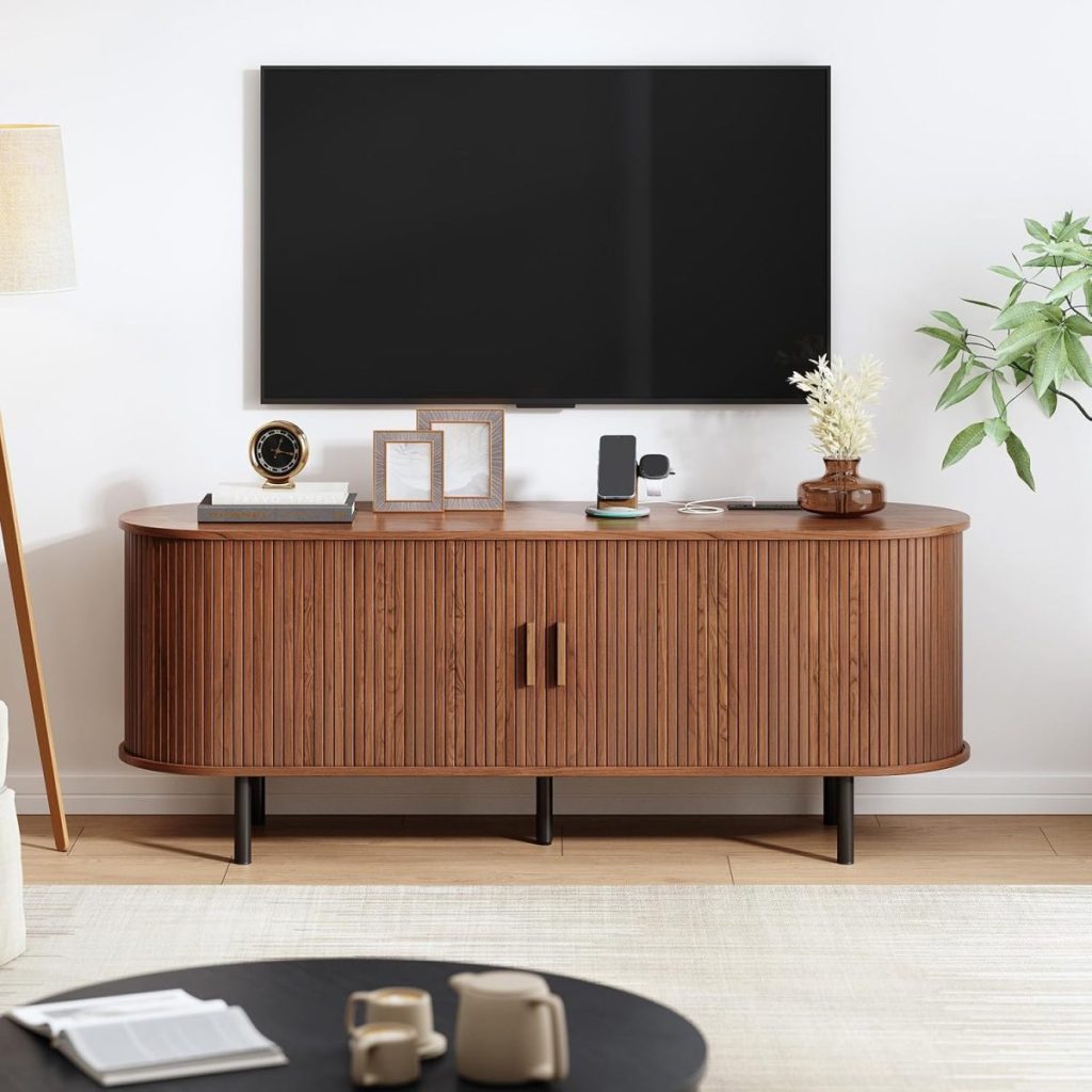 A wooden media console with a lamp, framed photos, decorative items, and electronics sits below a wall-mounted flat-screen TV in a modern living room—perfect for showcasing Black Friday finds.