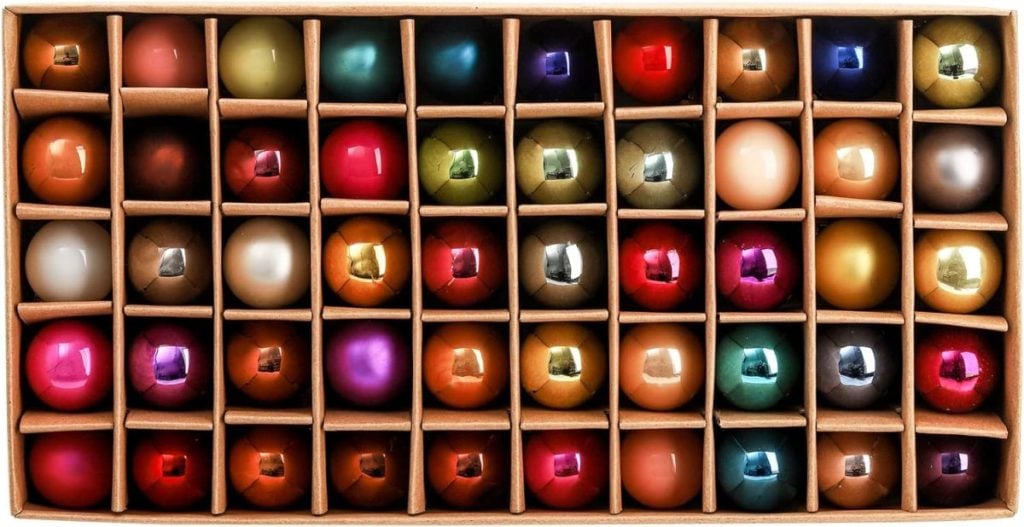 A box of assorted, multicolored Christmas ornaments, accented with festive Christmas ribbons, neatly arranged in five rows.