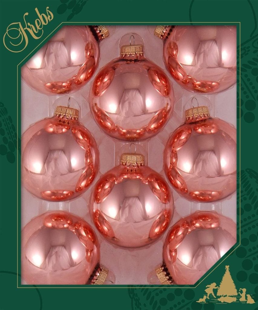 Nine shiny pink Christmas ornaments are elegantly arranged in a decorative box featuring a green border and gold accents, labeled "Krebs.