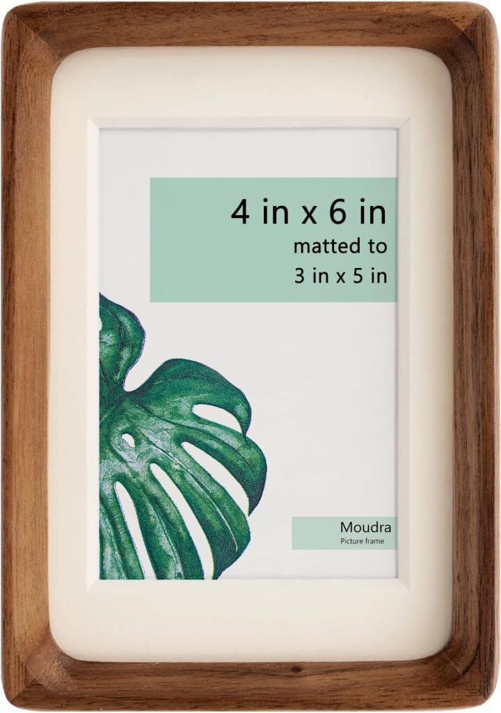 A wooden picture frame with a white mat, perfect for capturing Christmas Morning memories, displays a sign that reads "4 in x 6 in matted to 3 in x 5 in" alongside a green leaf graphic and the Moudra Picture Frame brand name.