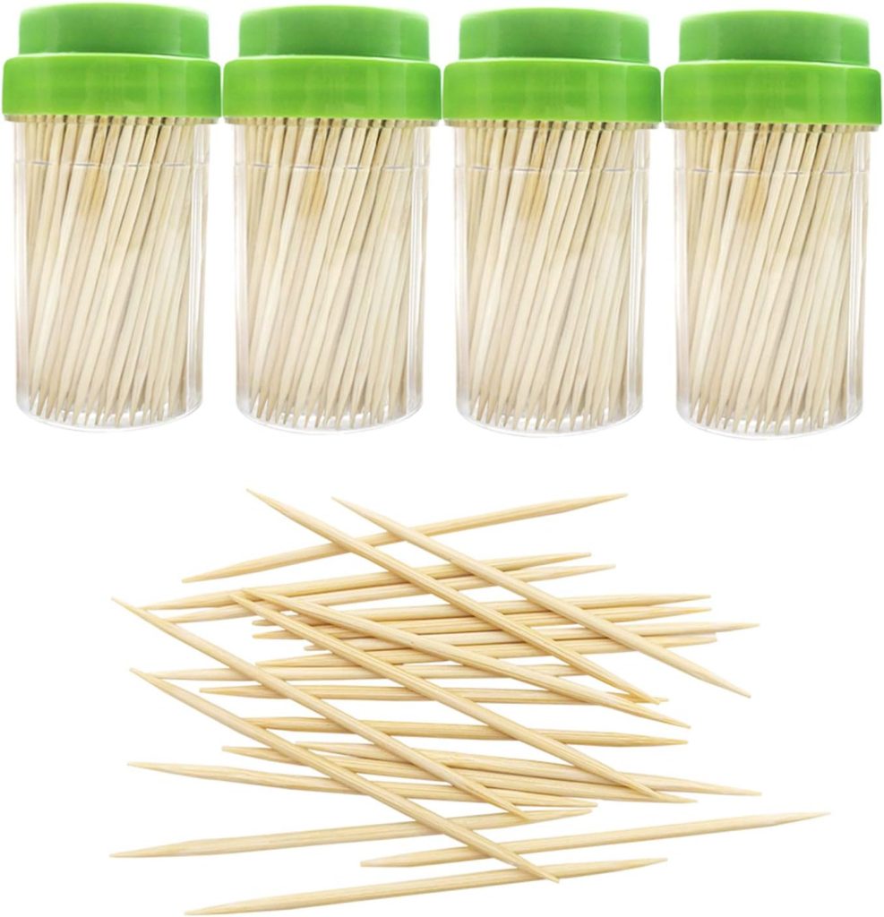 Four clear containers with green lids hold toothpicks, ready for crafting festive creations like Christmas tree cupcakes, with additional toothpicks scattered in the foreground.